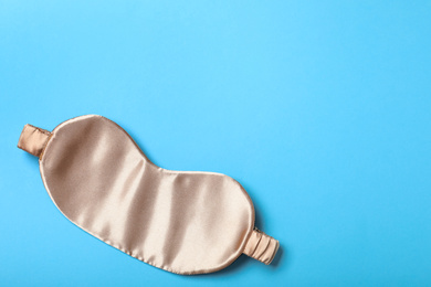 Beige sleeping mask on light blue background, top view with space for text. Bedtime accessory