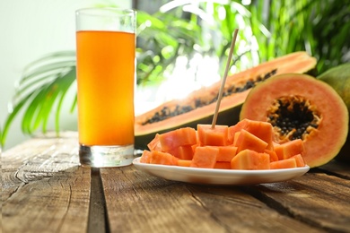 Photo of Fresh papayas and juice on wooden table against blurred background