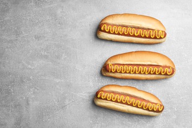 Photo of Fresh delicious hot dogs with mustard on light grey table, flat lay. Space for text