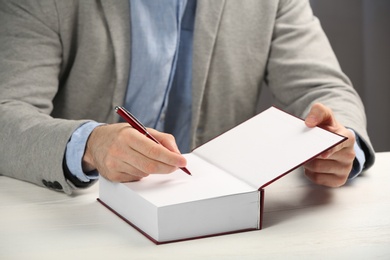 Photo of Writer signing autograph in book at table, closeup