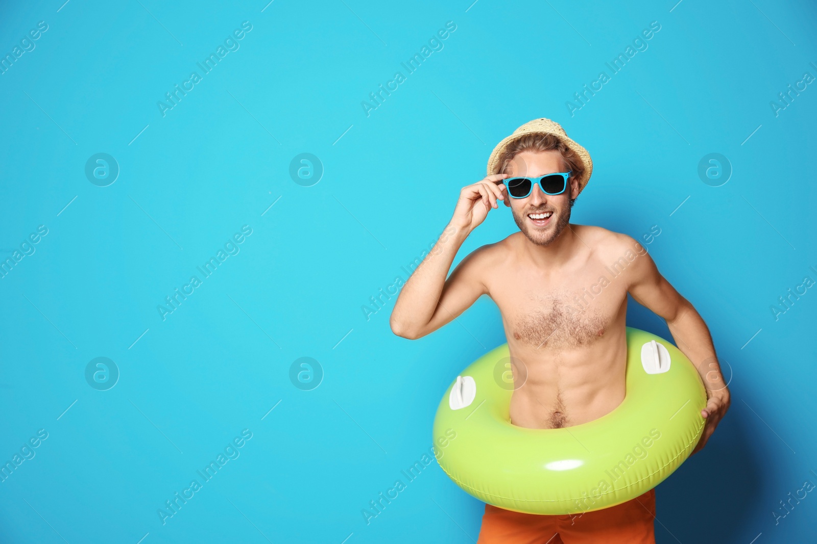 Photo of Young man in shorts with inflatable ring against color background. Space for text