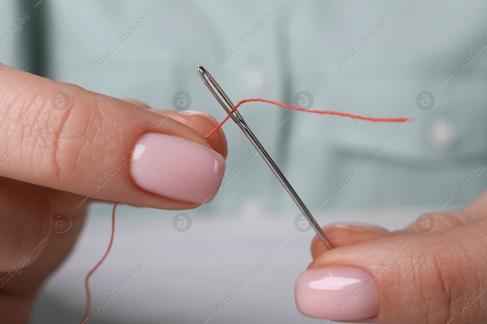 Photo of Woman threading sewing needle at table, closeup