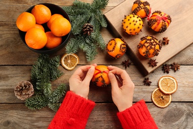Woman decorating fresh tangerine with red ribbon at wooden table, top view. Making Christmas pomander balls