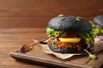 Board with tasty black vegetarian burger on wooden table