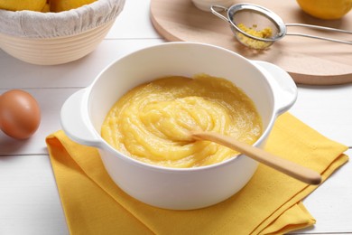 Delicious lemon curd in bowl, ingredients, spoon and sieve on white wooden table, closeup