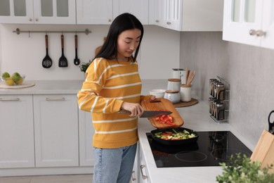 Photo of Cooking process. Beautiful woman adding cut bell pepper into pan with vegetables in kitchen. Space for text