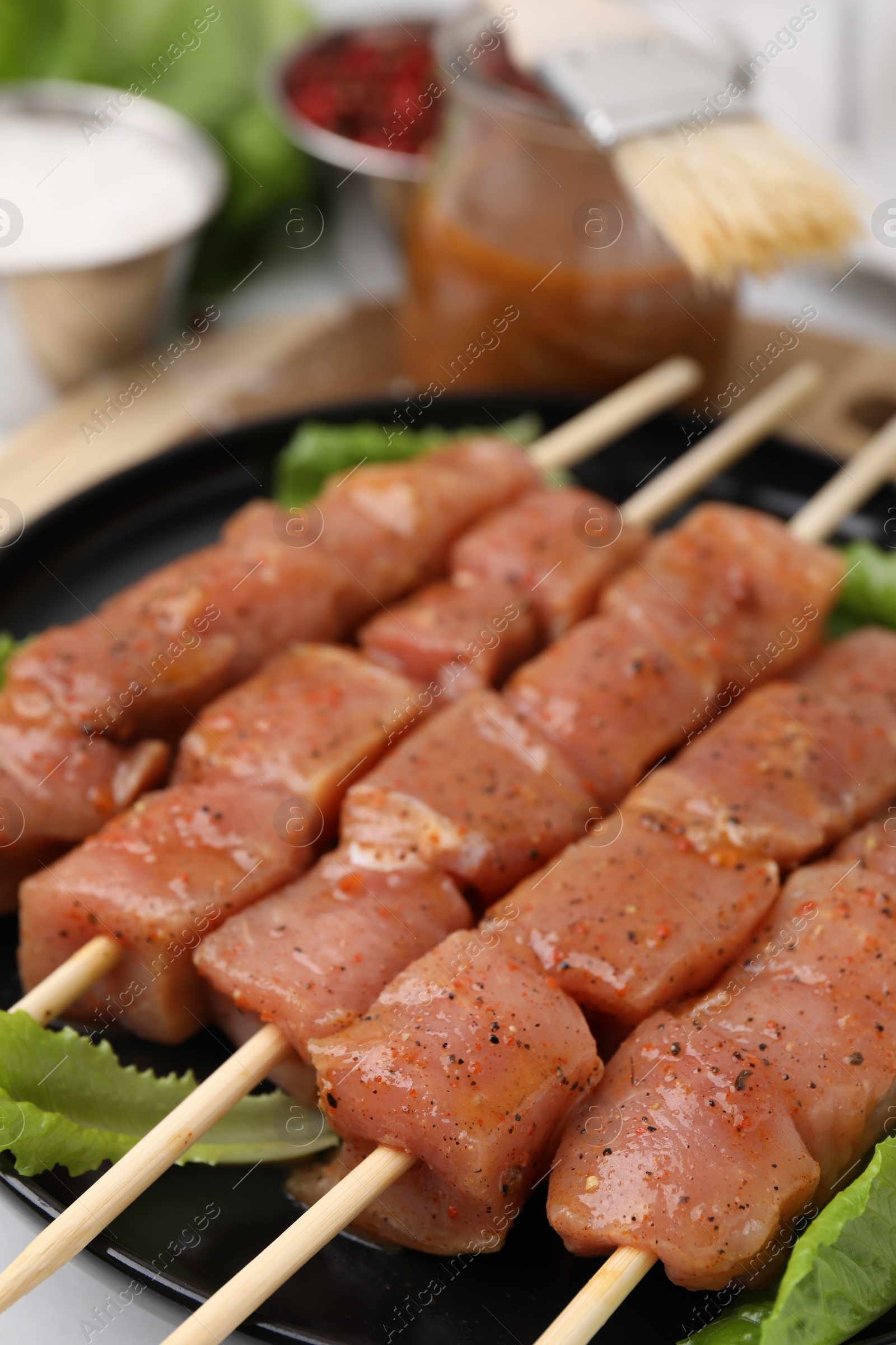 Photo of Wooden skewers with cut raw marinated meat on plate, closeup