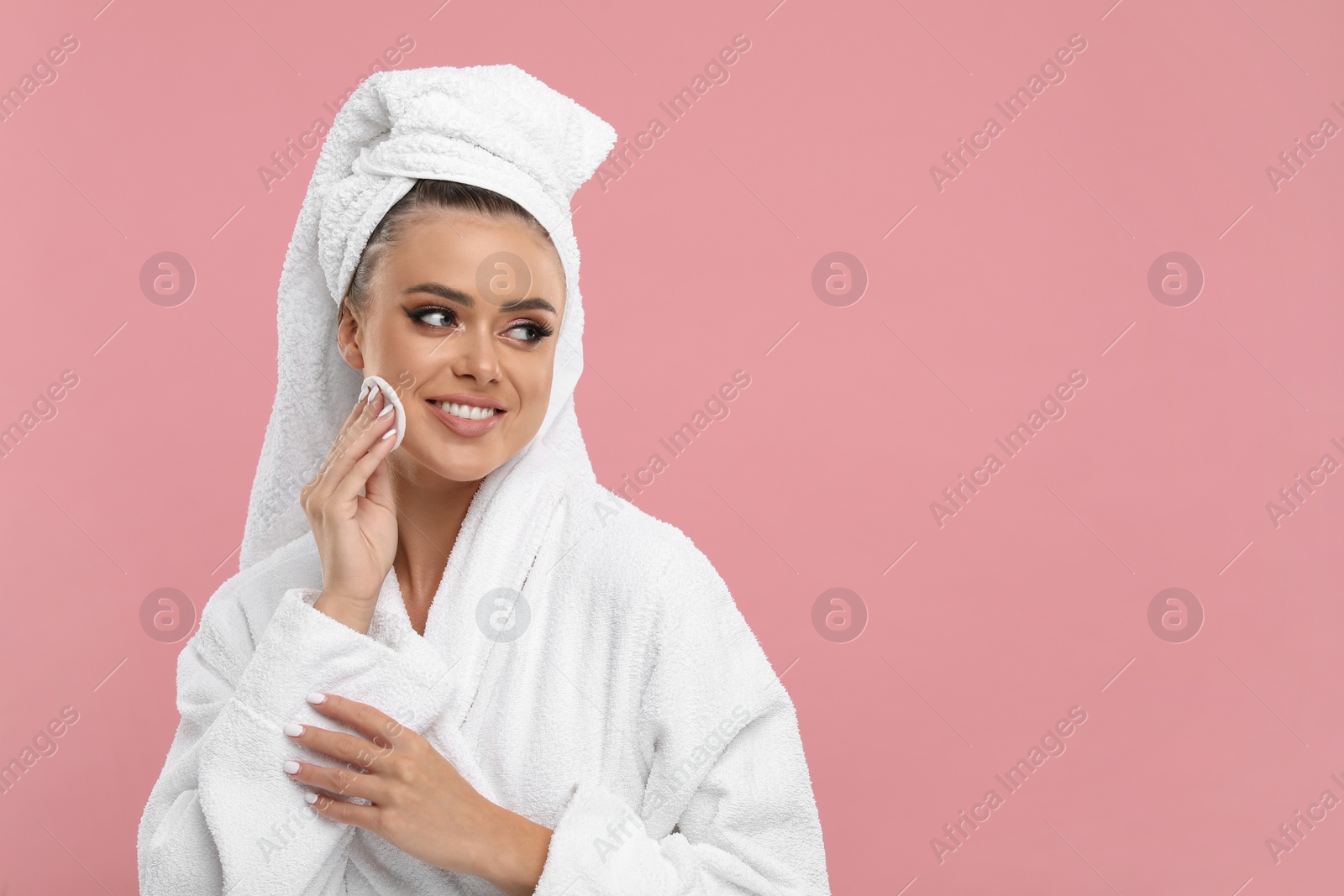 Photo of Beautiful woman removing makeup with cotton pad on pink background, space for text