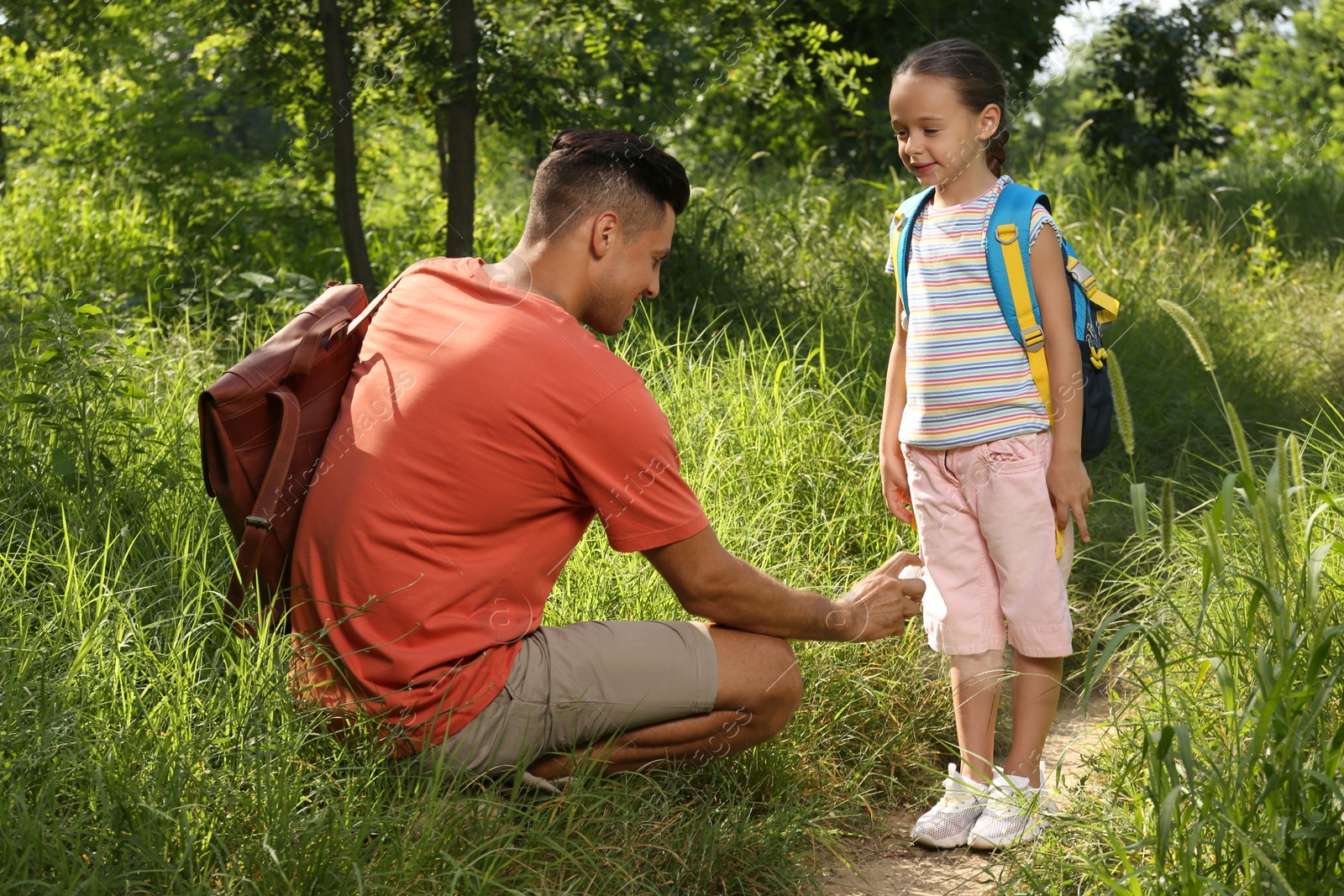 Photo of Father spraying tick repellent on his little daughter's legs during hike in nature