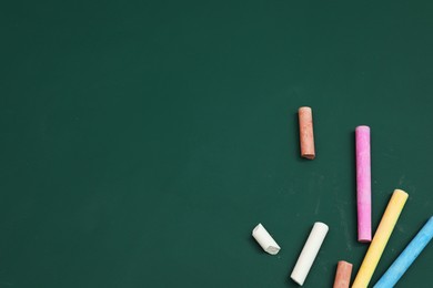 Photo of Colorful chalks on green board, flat lay. Space for text