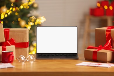 Laptop with blank screen, Christmas gifts and letters on table at home