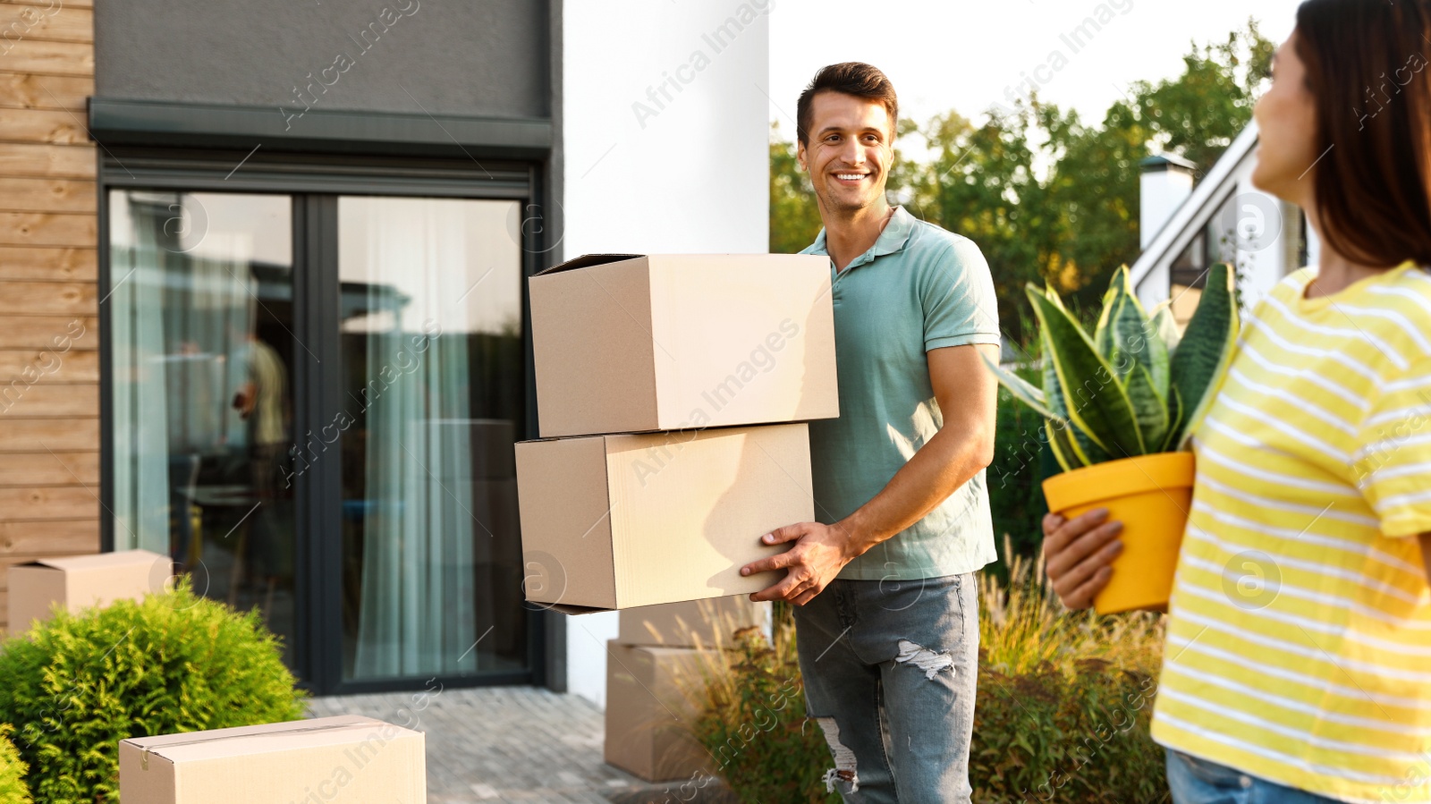 Photo of Happy couple with moving boxes and household stuff near their new house on sunny day