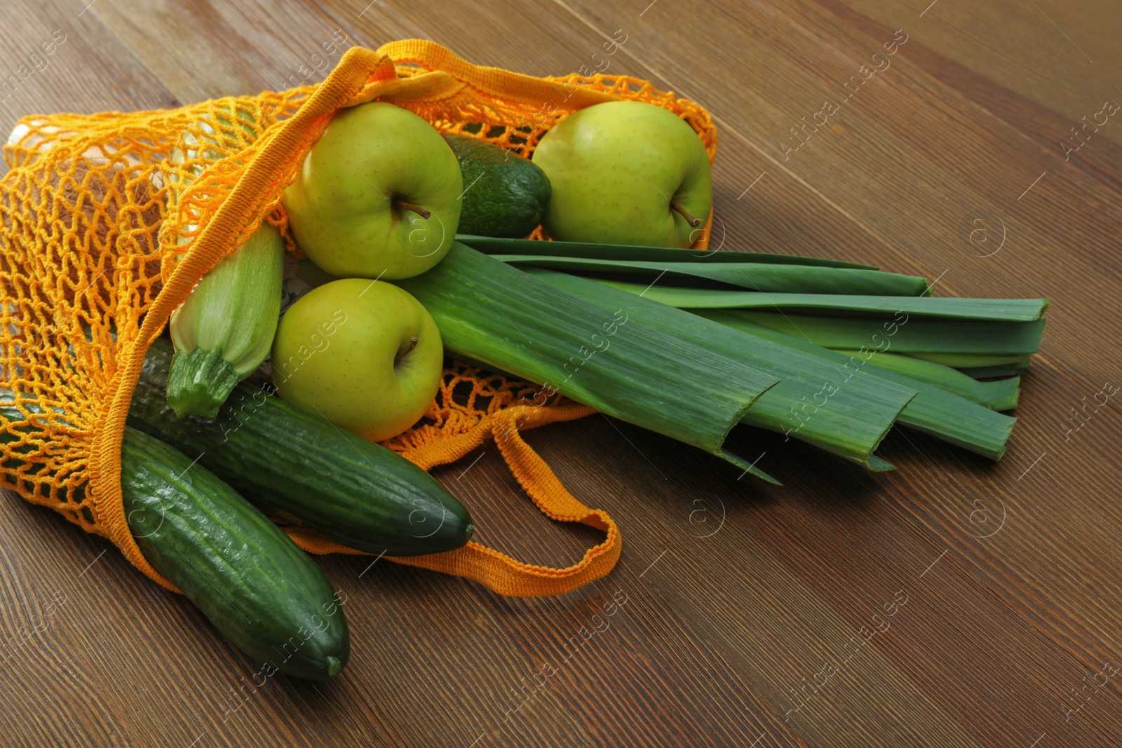 Photo of Net bag with vegetables and fruits on wooden table