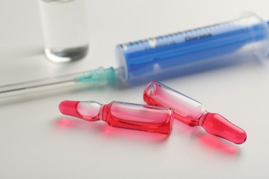 Photo of Glass ampoules with liquid and syringe on white background, closeup