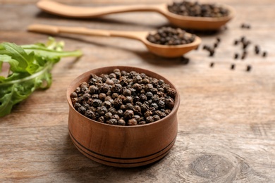 Bowl with black peppercorns on wooden table