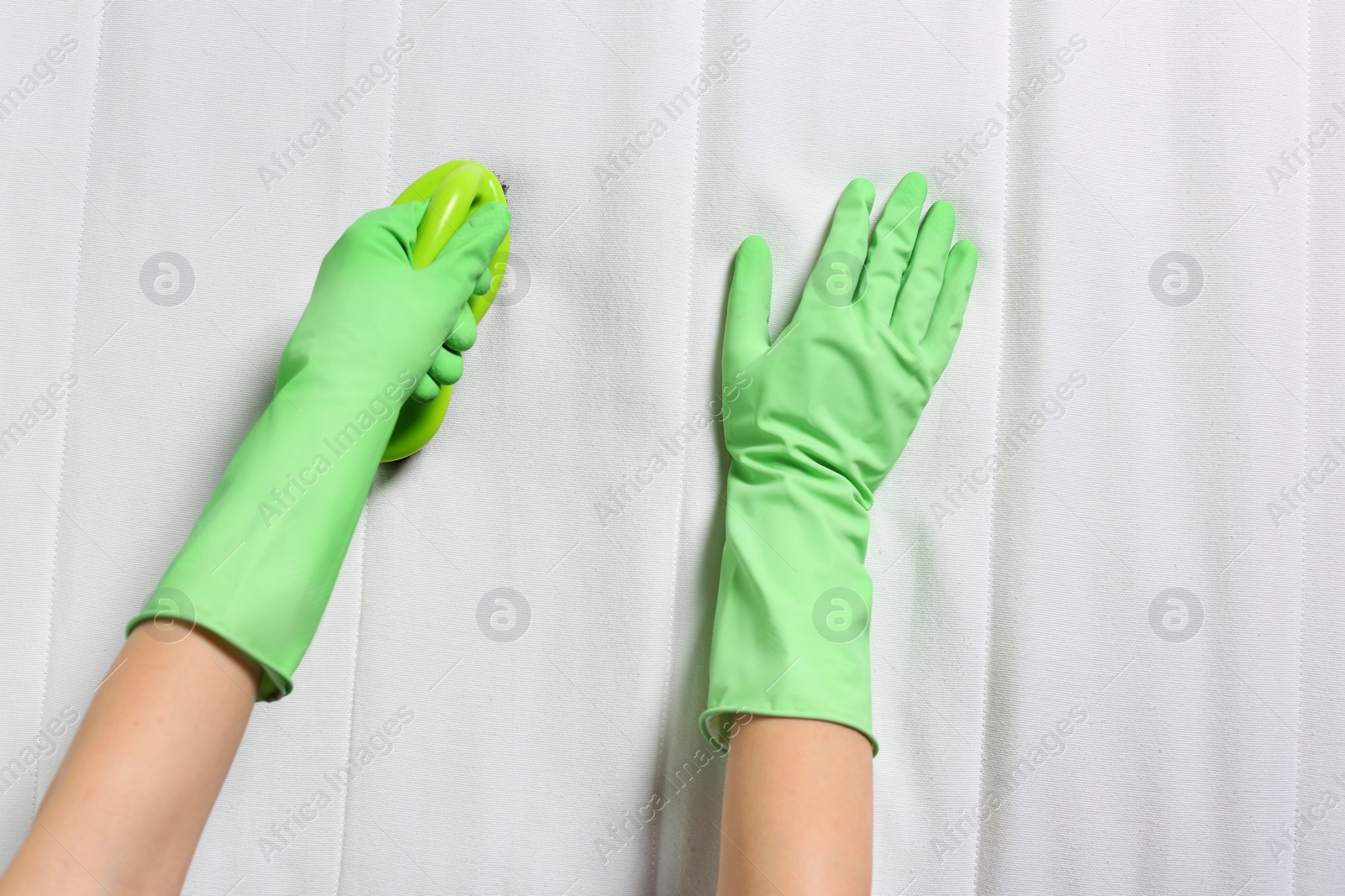 Photo of Woman in green gloves cleaning white mattress with brush, closeup