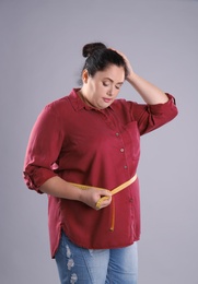 Photo of Fat woman with measuring tape on grey background. Weight loss