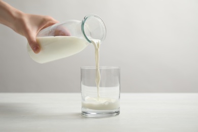 Photo of Woman pouring milk into glass at white table, closeup