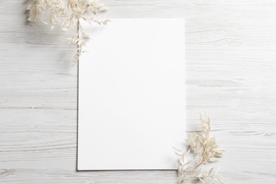 Photo of Empty sheet of paper and gypsophila flowers on white wooden table, flat lay. Mockup for design