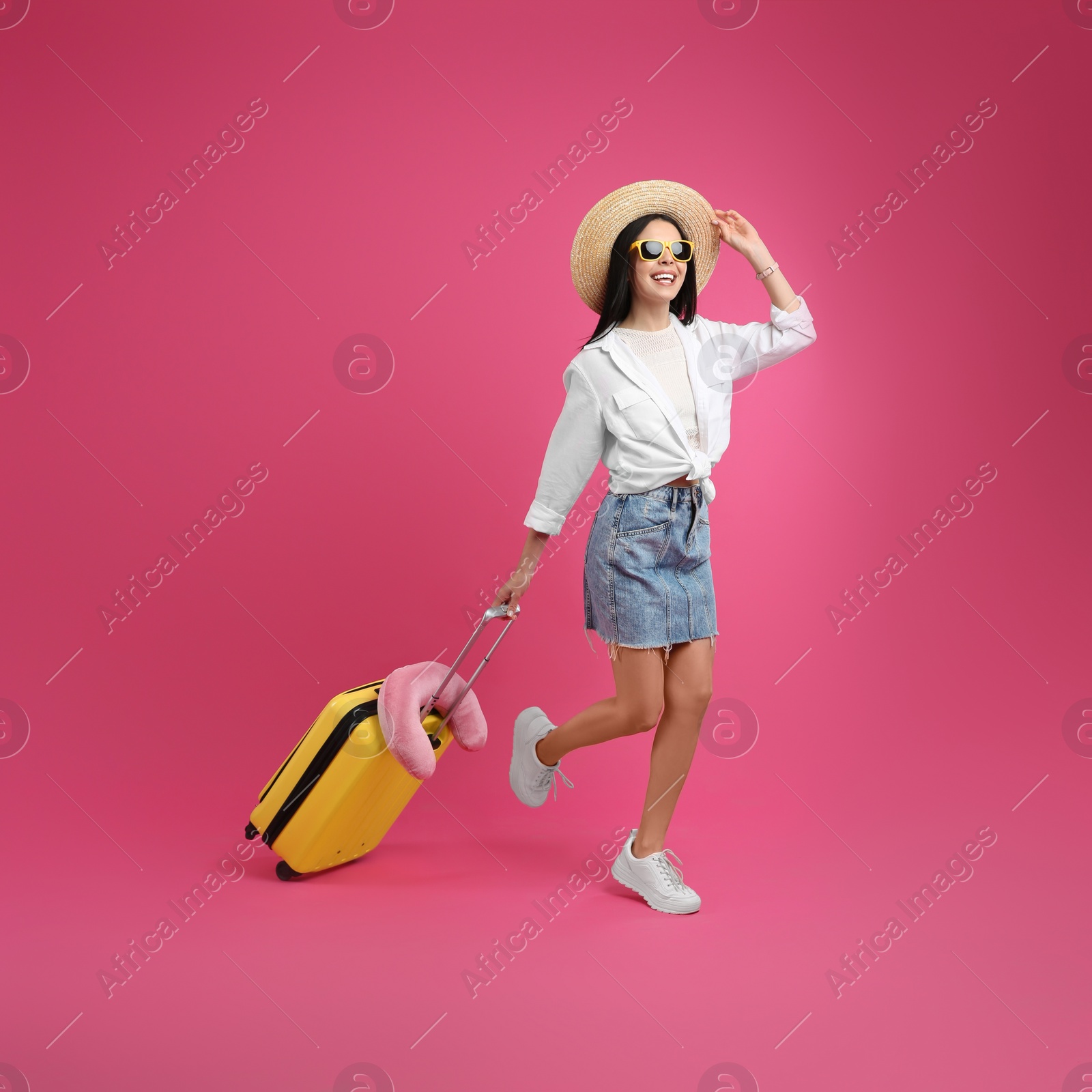 Photo of Happy female tourist with suitcase on pink background