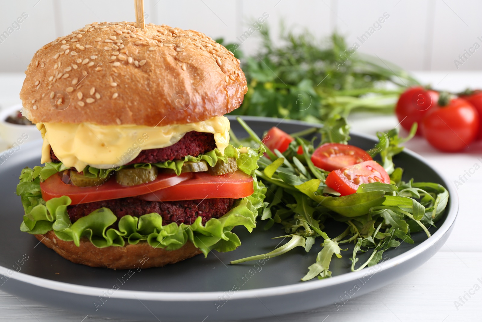 Photo of Delicious vegetarian burger served with salad on white wooden table, closeup