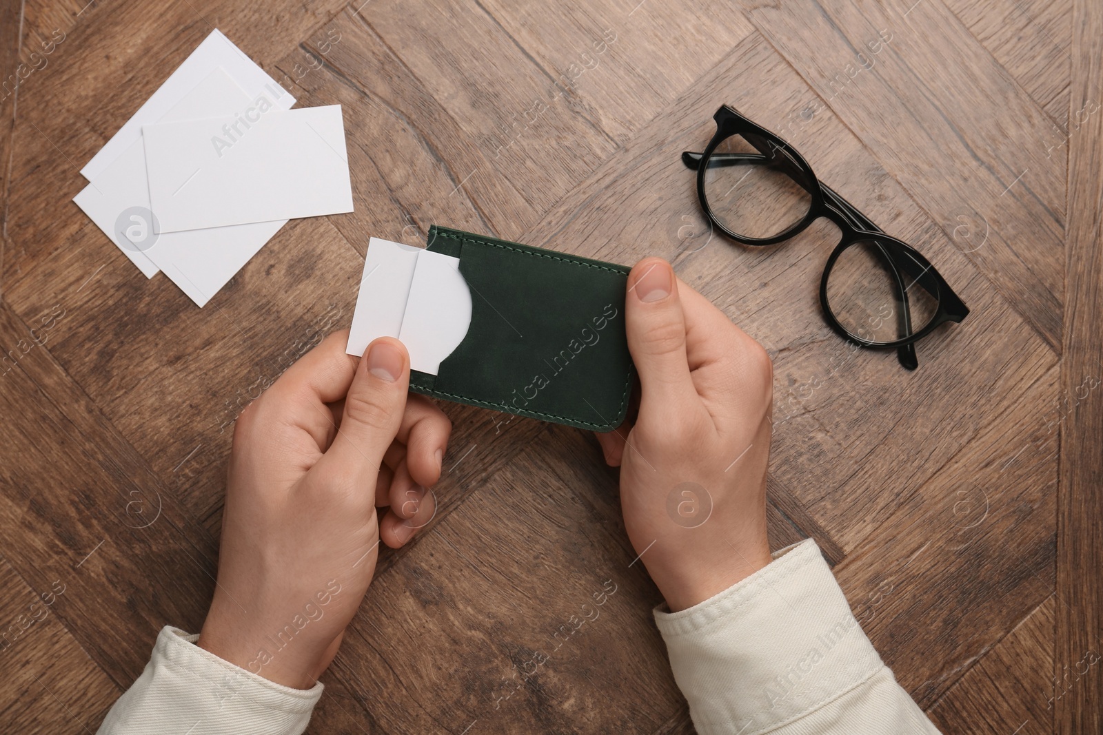 Photo of Man holding leather business card holder with blank cards at wooden table, top view