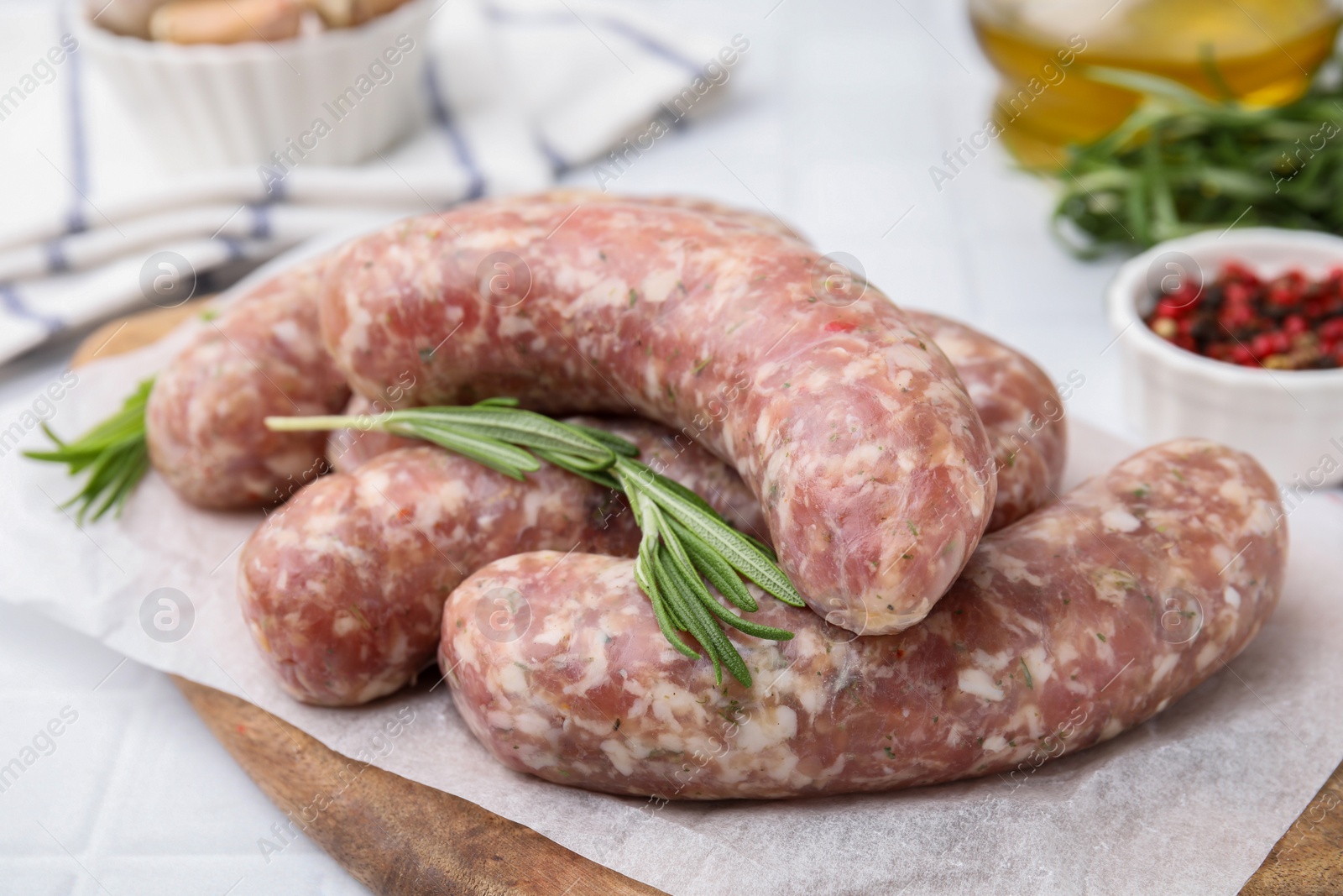 Photo of Raw homemade sausages and rosemary on white table, closeup