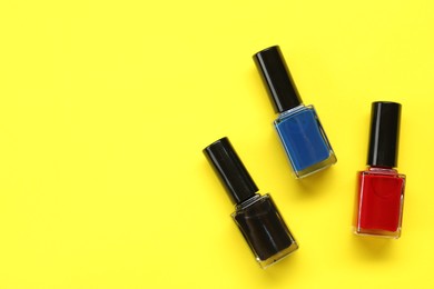 Colorful nail polishes in bottles on yellow background, flat lay. Space for text