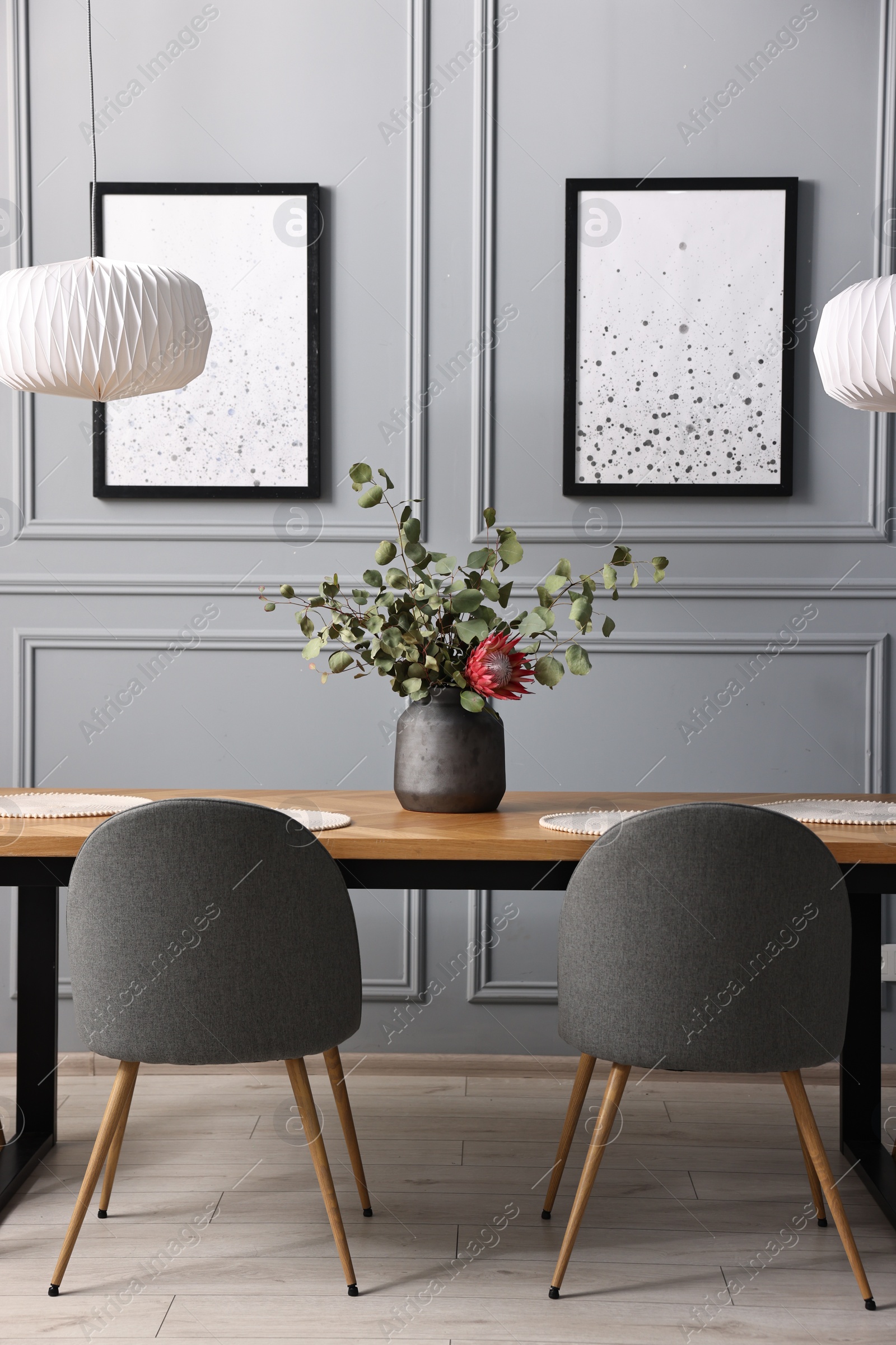 Photo of Soft chairs, table and vase with plants in stylish dining room