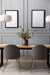 Photo of Soft chairs, table and vase with plants in stylish dining room