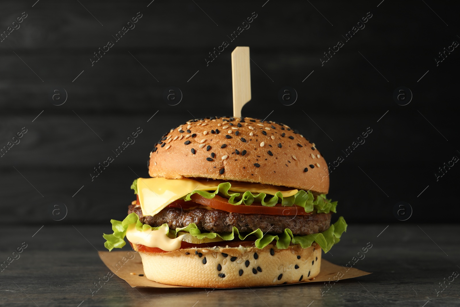 Burger with delicious patty on gray table against dark background Photo of Burger with delicious patty on gray table against dark background