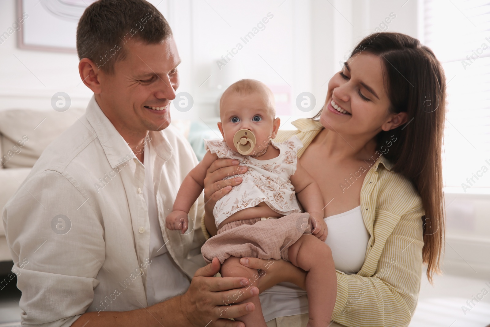 Photo of Happy couple holding their cute little baby with pacifier at home