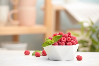 Bowl with ripe aromatic raspberries on table