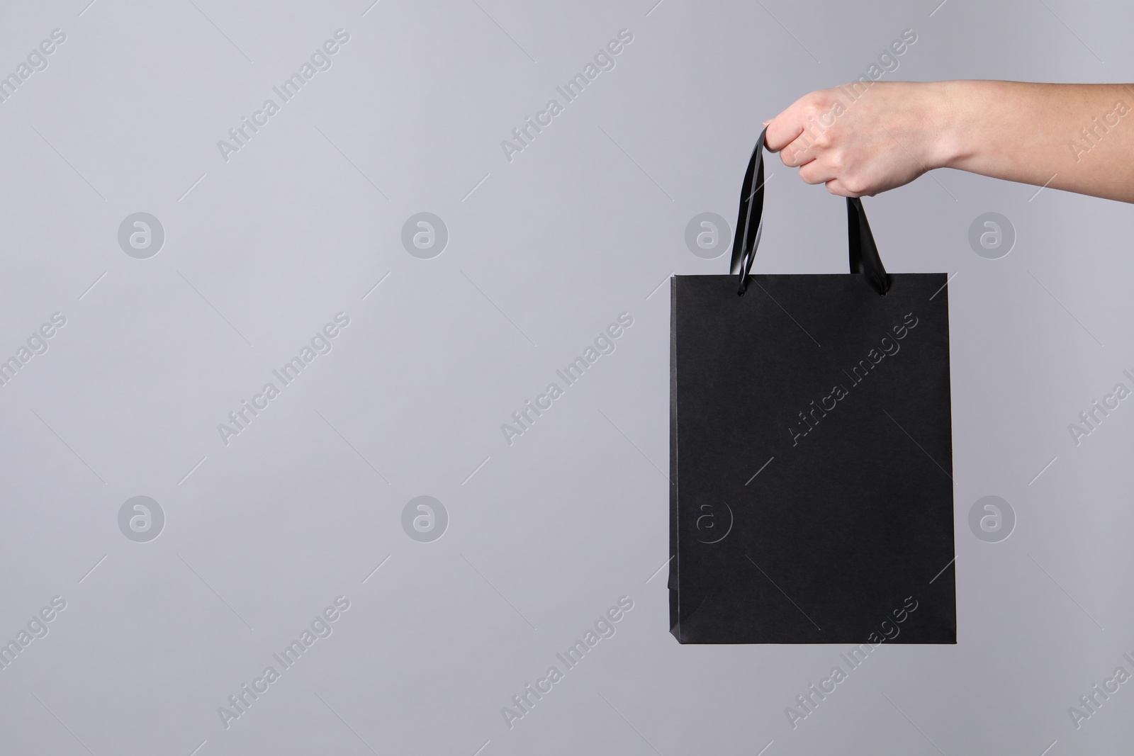 Photo of Woman holding paper shopping bag on grey background, closeup. Space for text