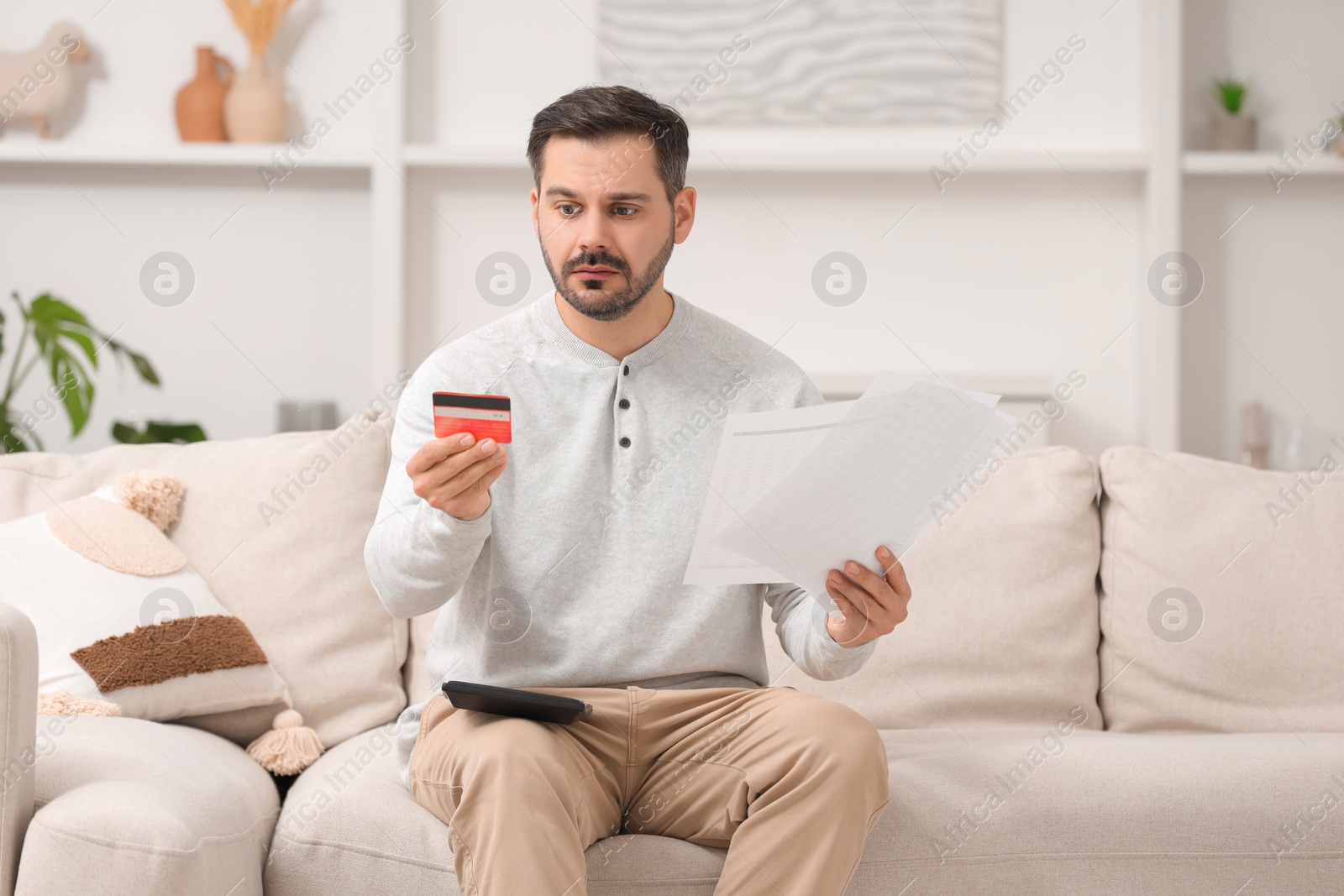 Photo of Confused man with debt notifications, calculator and credit card planning budget at home. Financial problem