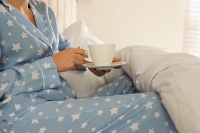 Photo of Woman with white cup and saucer in bed at home, closeup