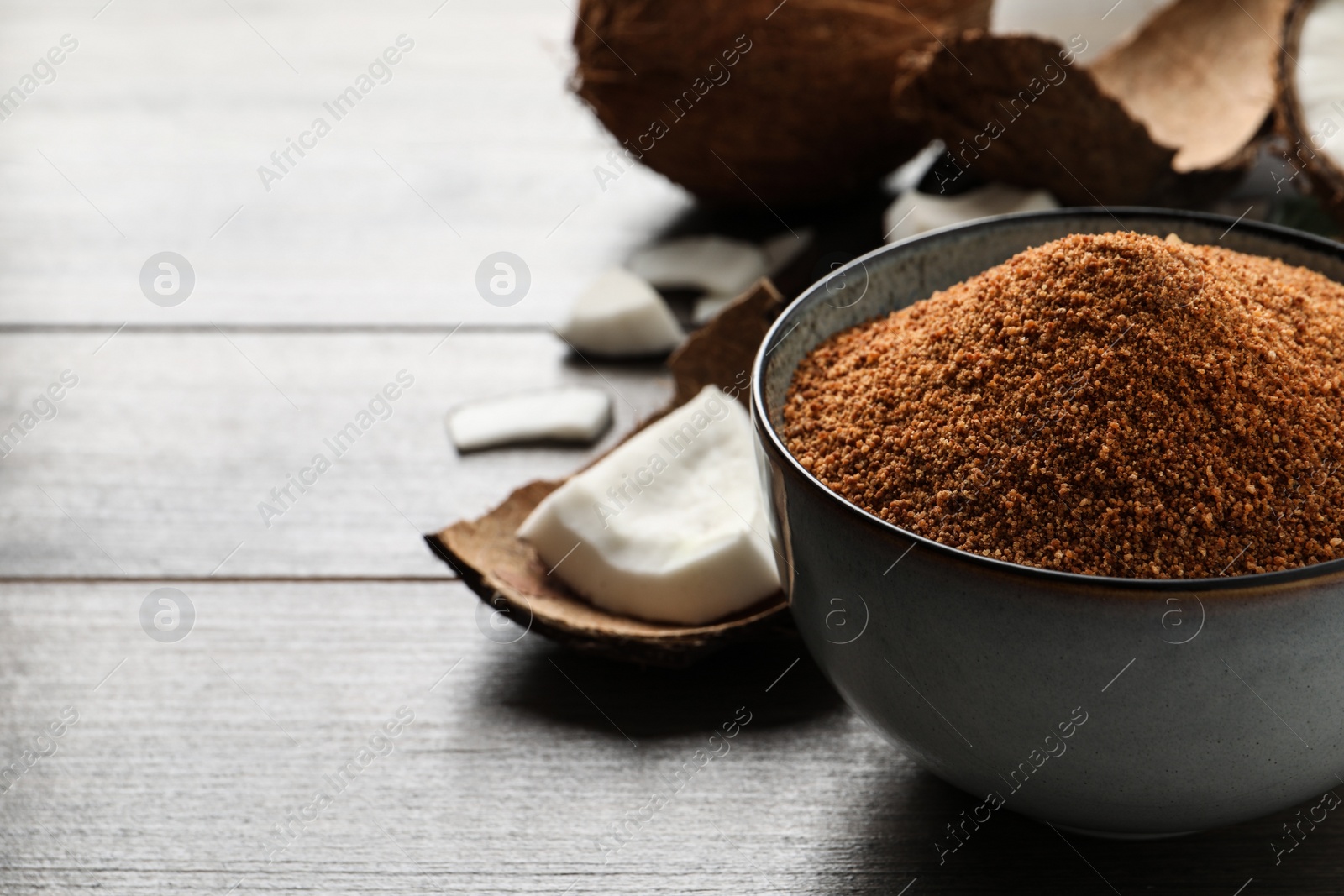 Photo of Natural coconut sugar in ceramic bowl on wooden table, space for text