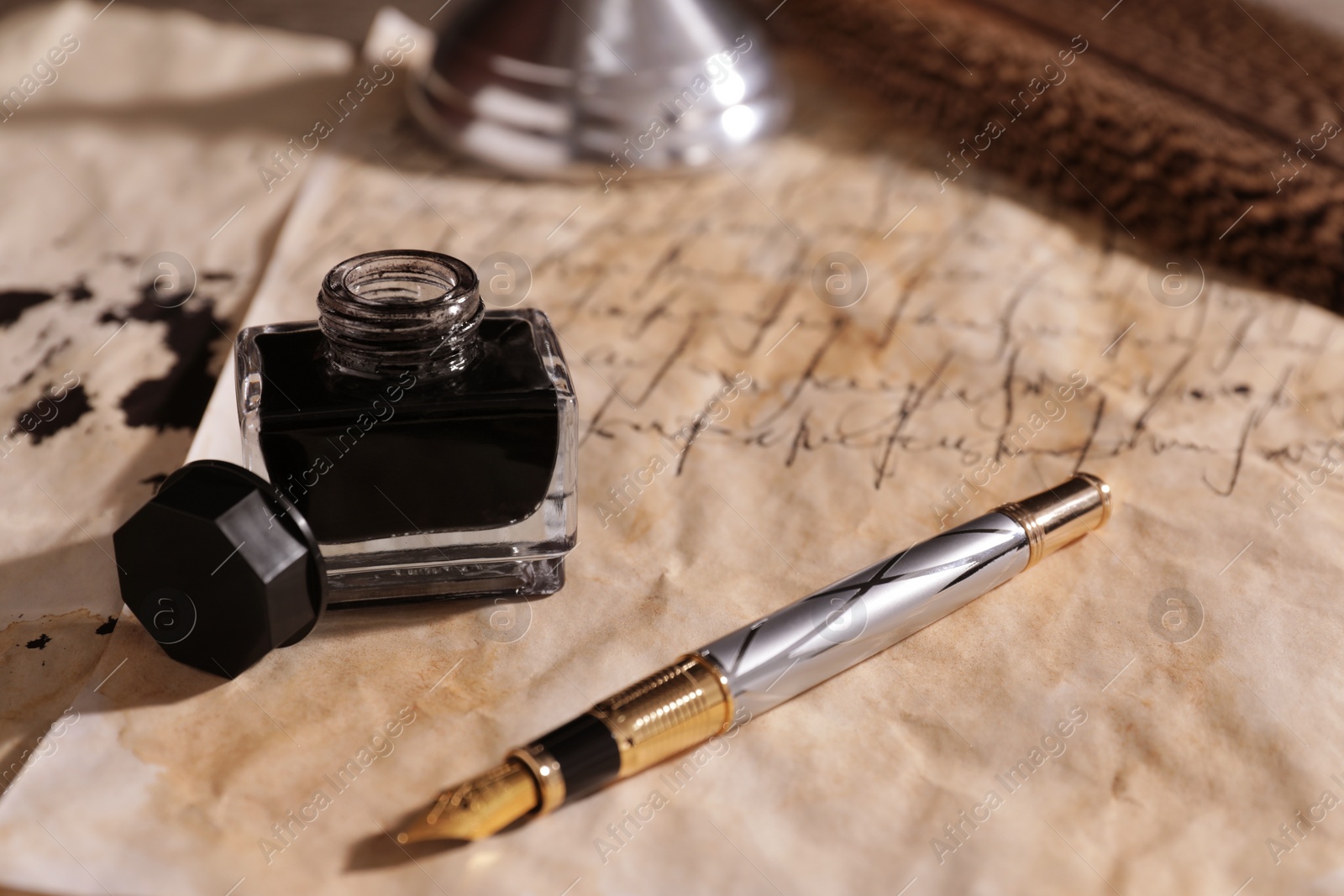 Photo of Open inkwell and fountain pen on vintage parchment with text, closeup