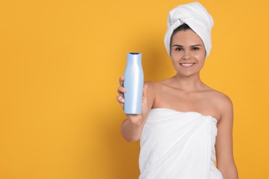 Photo of Beautiful young woman holding bottle of shampoo on orange background, space for text
