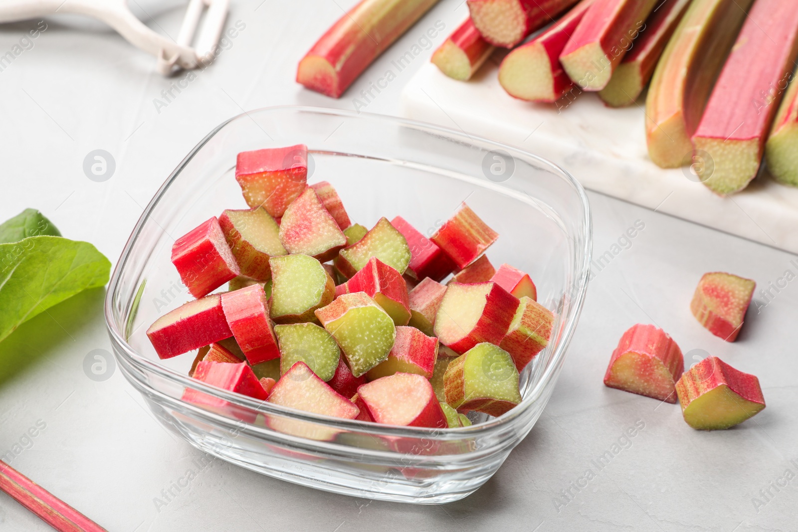 Photo of Whole and cut rhubarb stalks on white table, closeup