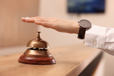 Photo of Woman ringing service bell at wooden reception desk in hotel, closeup