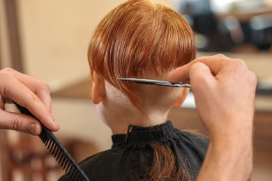 Professional hairdresser cutting boy's hair in beauty salon, closeup