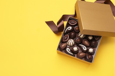 Photo of Open box of delicious chocolate candies on yellow background, flat lay. Space for text