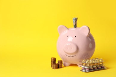 Photo of Piggy bank with money and pills on yellow background, space for text. Medical insurance