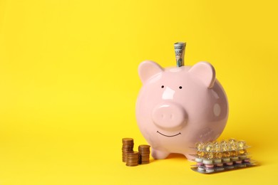 Piggy bank with money and pills on yellow background, space for text. Medical insurance