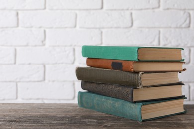 Photo of Stack of old hardcover books on wooden table near white brick wall, space for text