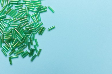 Pile of green bugle beads on light blue background, flat lay. Space for text