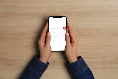 Image of New message notification. Woman with mobile phone at wooden table, top view