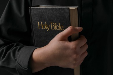 Photo of Woman with holy Bible on black background, closeup
