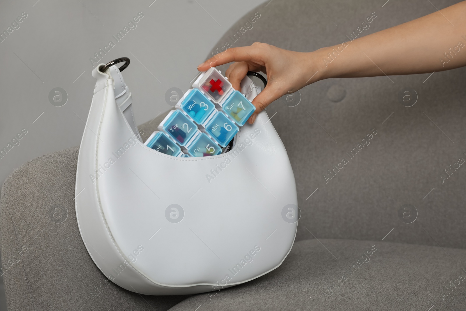 Photo of Woman putting plastic box with pills into bag on sofa indoors, closeup